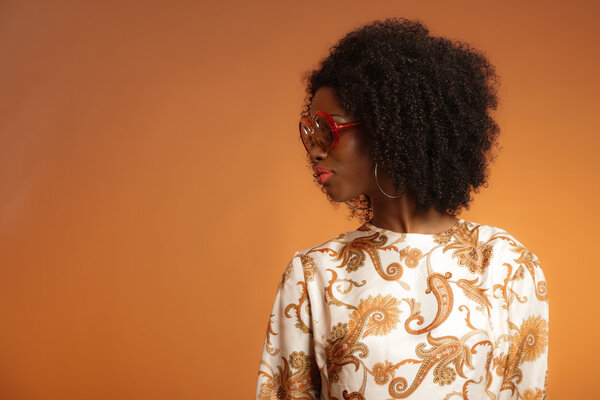 Retro 70s fashion african woman with paisley dress and sunglasses. Brown background.