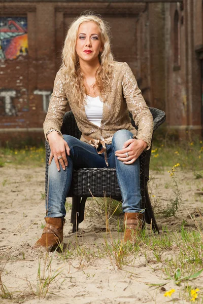 Pretty blonde fashion girl sitting in chair outdoor in urban env — Stock Photo, Image