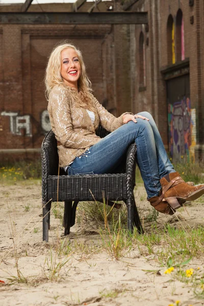 Pretty blonde fashion girl sitting in chair outdoor in urban env — Stock Photo, Image