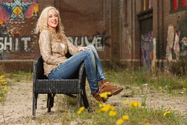 Pretty blonde fashion girl sitting in chair outdoor in urban env — Stock Photo, Image
