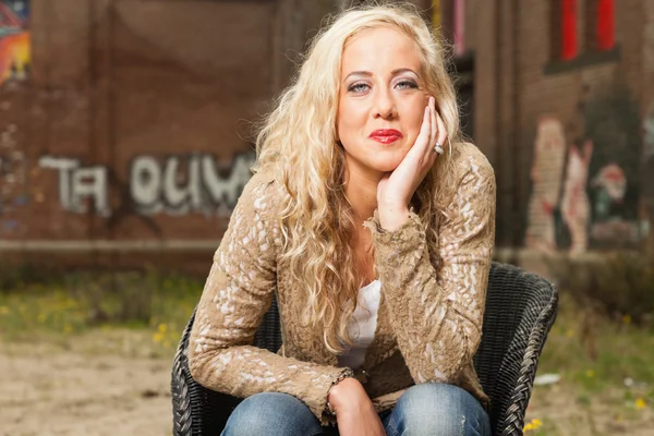 Söt blond flicka sitter i stol utomhus i urban miljö — Stockfoto