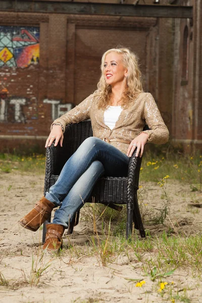 Mooie blonde mode meisje zit in een stoel buiten in stedelijke env — Stockfoto