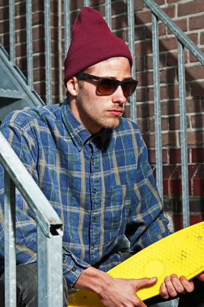 Skateboarder urbano con cappello di lana e occhiali da sole tenendo il suo bo — Foto Stock