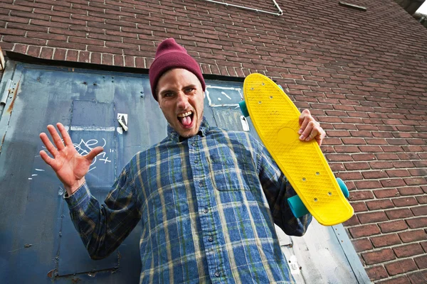 Wahnsinniger ausdrucksstarker Skateboarder mit Wollmütze, der sein Skateboa hält — Stockfoto