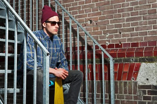 Skatista urbano com chapéu de lã e óculos de sol segurando seu bo — Fotografia de Stock