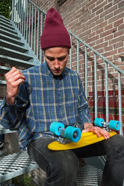 Urban skateboarder with woolen hat checking wheels of his skateb — Stock Photo, Image