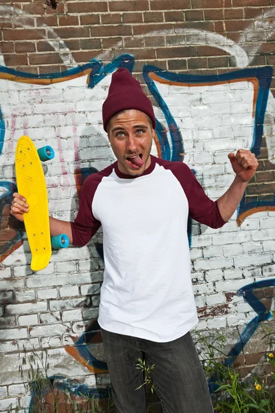 Crazy expressive skateboarder with woolen cap in front of graffi — Stock Photo, Image