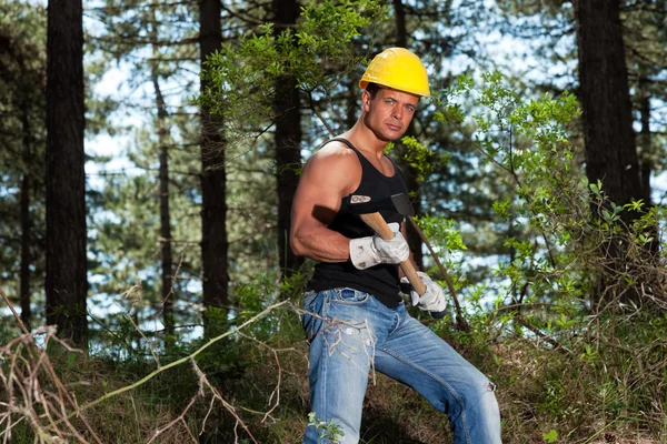 Muscled lumberjack with black shirt and axe in forest. Wearing y — Stock Photo, Image