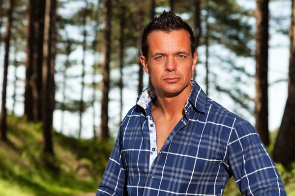 Hombre leñador bien parecido con camisa azul en el bosque . —  Fotos de Stock