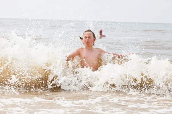 Egy fiatal fiú, lejátszás, hullámok az óceánon. — Stock Fotó