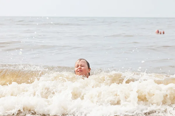 Um menino brincando no oceano com ondas . — Fotografia de Stock