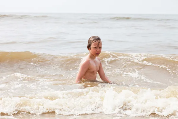 Um menino brincando no oceano com ondas . — Fotografia de Stock