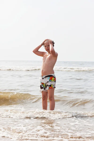 Jonge jongen permanent in het water aan het strand. — Stockfoto