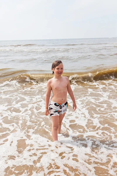 Kid jongen plezier op het strand in de golven van de Oceaan. — Stockfoto
