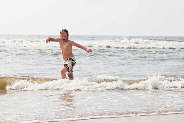 Jonge jongen permanent in het water aan het strand. — Stockfoto