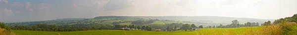 Fjelllandskap med enger og trær og blå skyet himmel. Panora – stockfoto