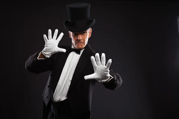 Magician making mysterious gestures. Wearing black suit and hat. — Stock Photo, Image