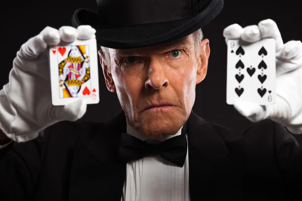 Magician with black suit and hat holding set of cards. Studio sh — Stock Photo, Image