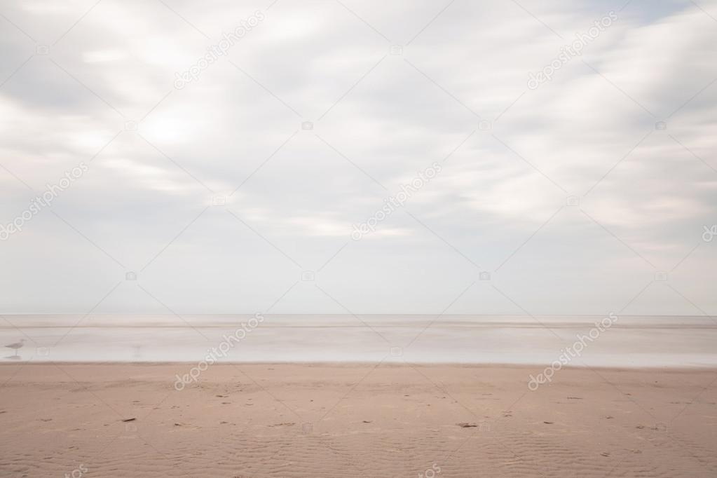 Long exposure shot of beach with blue cloudy sky.