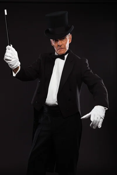 Magician with black suit and hat holding a magic stick. Studio s — Stock Photo, Image