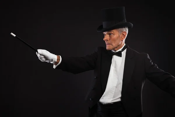 Magician with black suit and hat holding a magic stick. Studio s — Stock Photo, Image