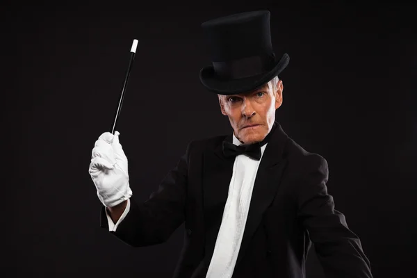 Mago con traje negro y sombrero sosteniendo un palo mágico. Estudio s —  Fotos de Stock