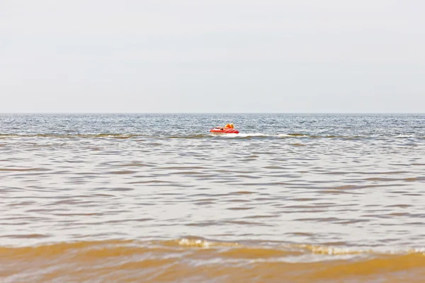 Um miúdo com um anel de borracha a andar depressa atrás de um barco no oceano. A divertir-me — Fotografia de Stock