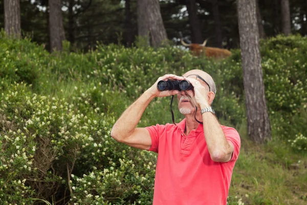 Senior retired man with beard using binoculars outdoors. Wearing — Stock Photo, Image