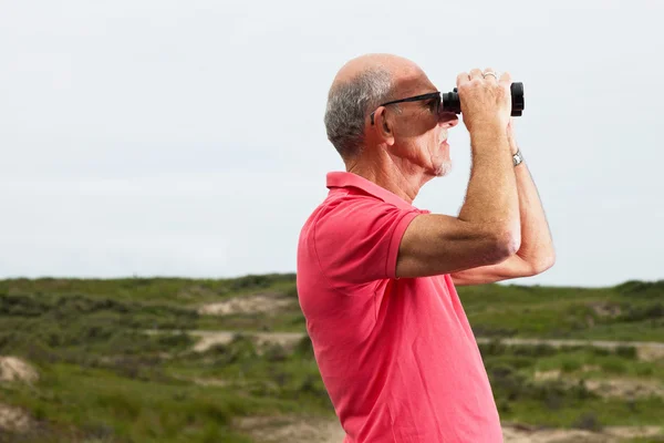 Pensionerad man med skägg och glasögon med kikare utomhus i — Stockfoto