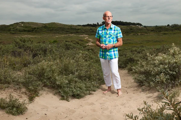 Homem idoso aposentado andando ao ar livre na paisagem duna grama. Wea... — Fotografia de Stock