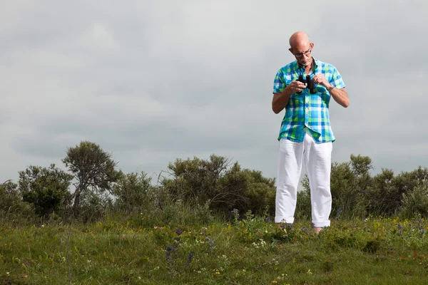 Hombre mayor con barba y gafas usando prismáticos al aire libre en g — Foto de Stock