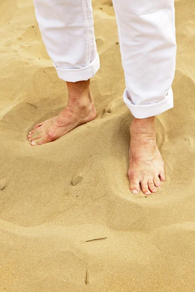 Füße eines älteren Mannes, der im Sand steht. trägt weiße Hose. — Stockfoto