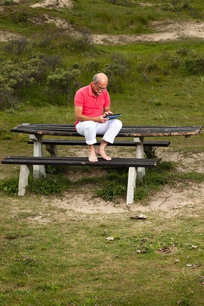 Pensionerade ledande man vilar och använder sin tablett vid bord i park — Stockfoto