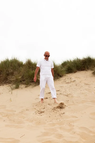 Retired man with beard and sunglasses walking in grass dune land — Stock Photo, Image