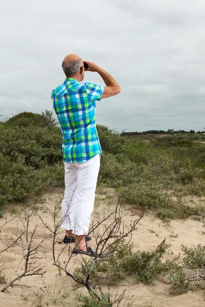 Senior man with beard and glasses using binoculars outdoors in g — Stock Photo, Image