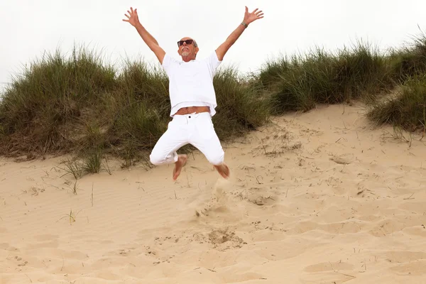 Jumping happy retired man with beard and sunglasses in grass dun — Stock Photo, Image