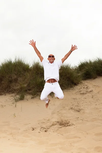 Прыгающий счастливый пенсионер с бородой и солнцезащитными очками в траве — стоковое фото