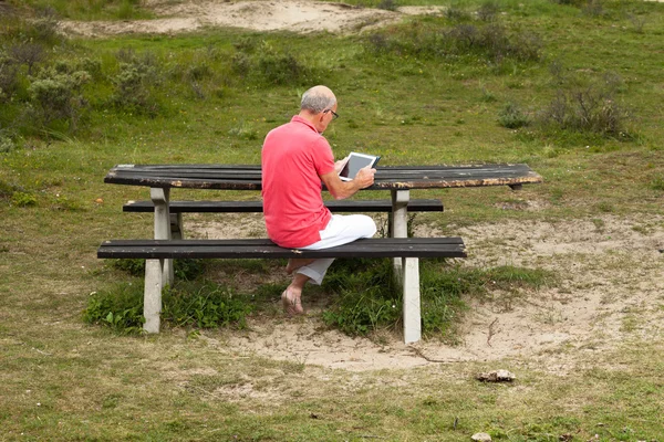 Pensionerade ledande man vilar och använder sin tablett vid bord i park — Stockfoto