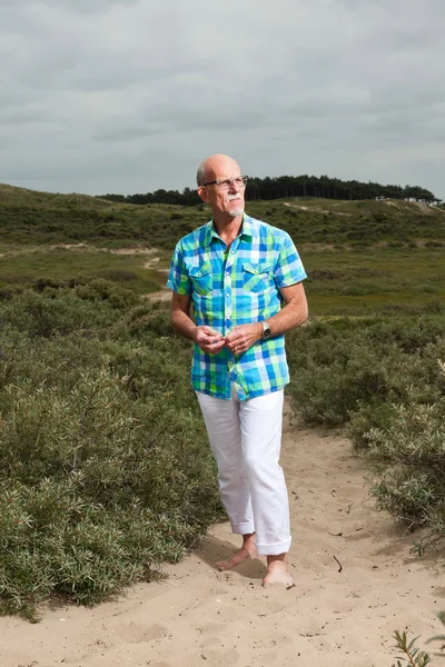 Homem idoso aposentado andando ao ar livre na paisagem duna grama. Wea... — Fotografia de Stock