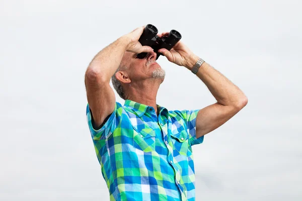 Senior man with beard and glasses using binoculars outdoors in g — Stock Photo, Image