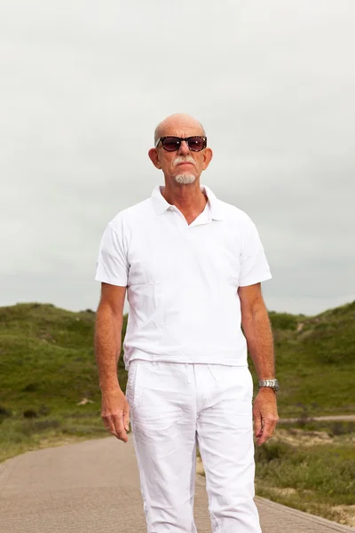 Retired senior man with beard and sunglasses walking outdoors in — Stock Photo, Image