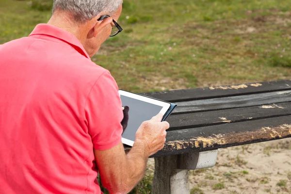 Rentner ruht sich aus und bedient sein Tablet am Tisch im Park — Stockfoto