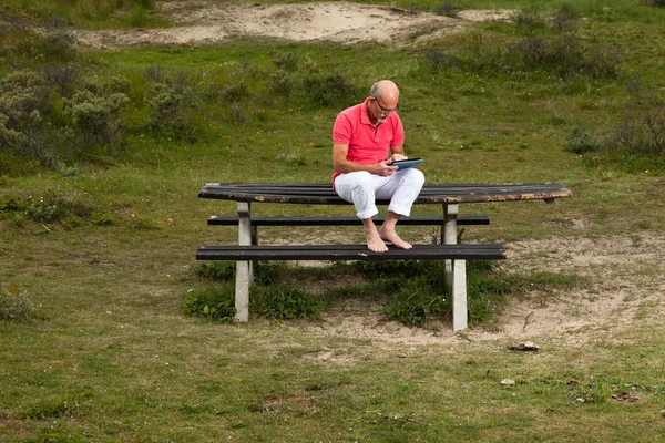 Pensionerade ledande man vilar och använder sin tablett vid bord i park — Stockfoto