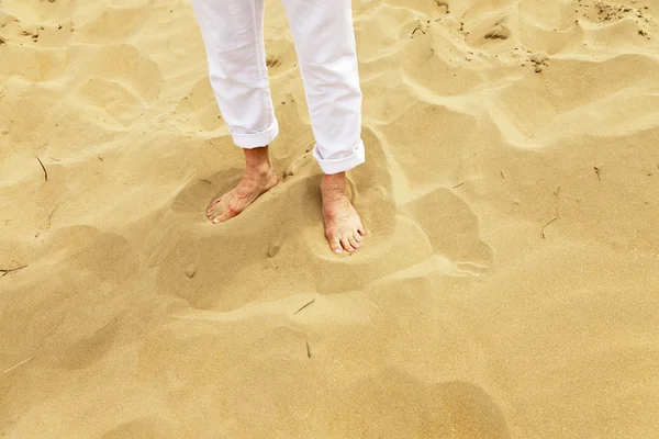 Füße eines älteren Mannes, der im Sand steht. trägt weiße Hose. — Stockfoto