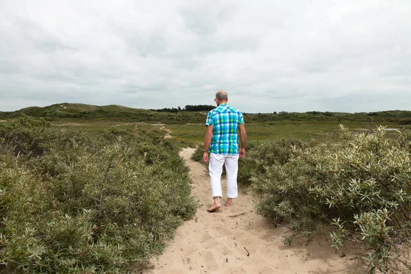 Jubilado hombre mayor caminando en el paisaje de dunas de hierba con s nublado — Foto de Stock