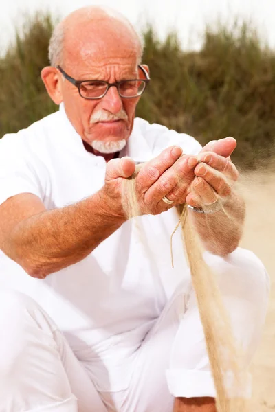 Voormalig senior man met zand uit zijn handen vallen. — Stockfoto