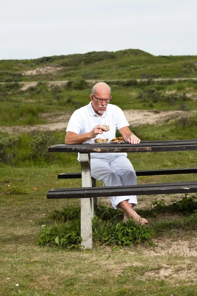 Pensionerad man med skägg och glasögon vila och äta lunch i g — Stockfoto