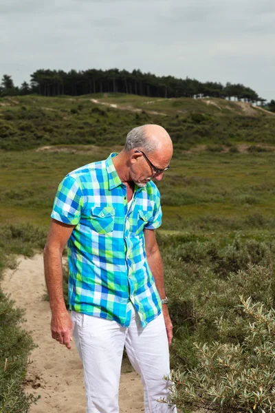 Retired senior man walking outdoors in grass dune landscape. Wea — Stock Photo, Image