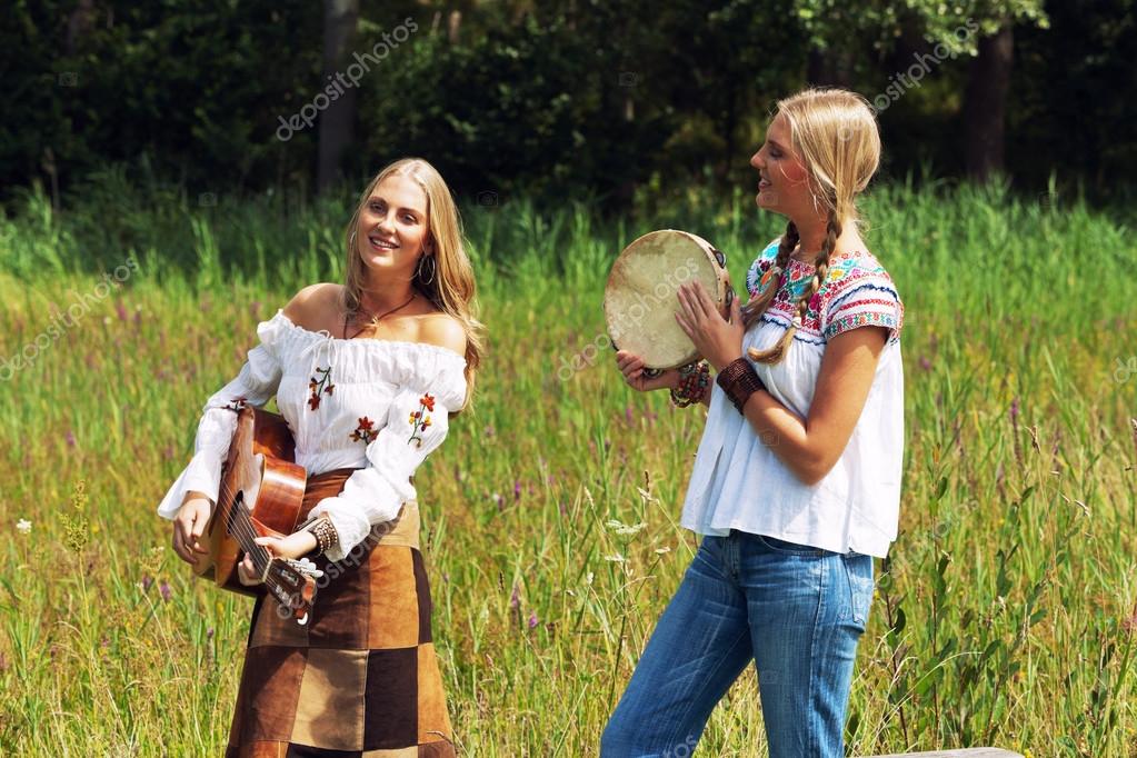 Two retro blonde 70s hippie girls making music with acoustic guitar and  tambourine outdoor in nature. Stock Photo by ©ysbrand 30258567