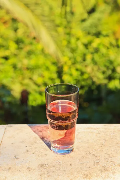 Glass of fresh pink soda on balcony with blurred green garden ba — Stock Photo, Image